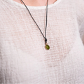 Person wearing a necklace with a green pendant on a plain background