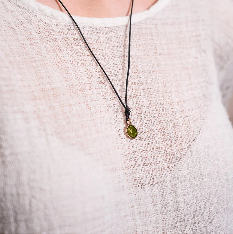 Person wearing a necklace with a green pendant on a plain background