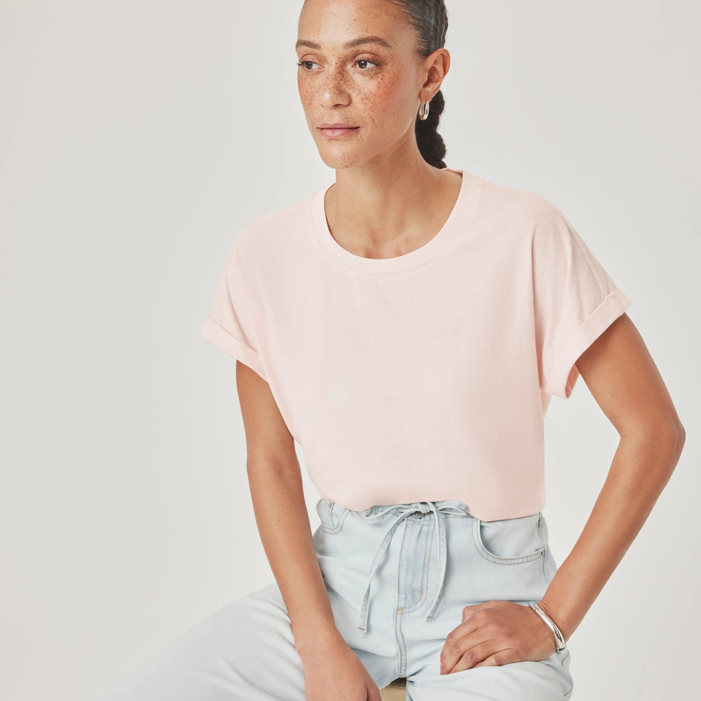 A woman wearing a light pink short-sleeve crewneck t-shirt and light blue high-waisted jeans, seated against a light gray studio background.