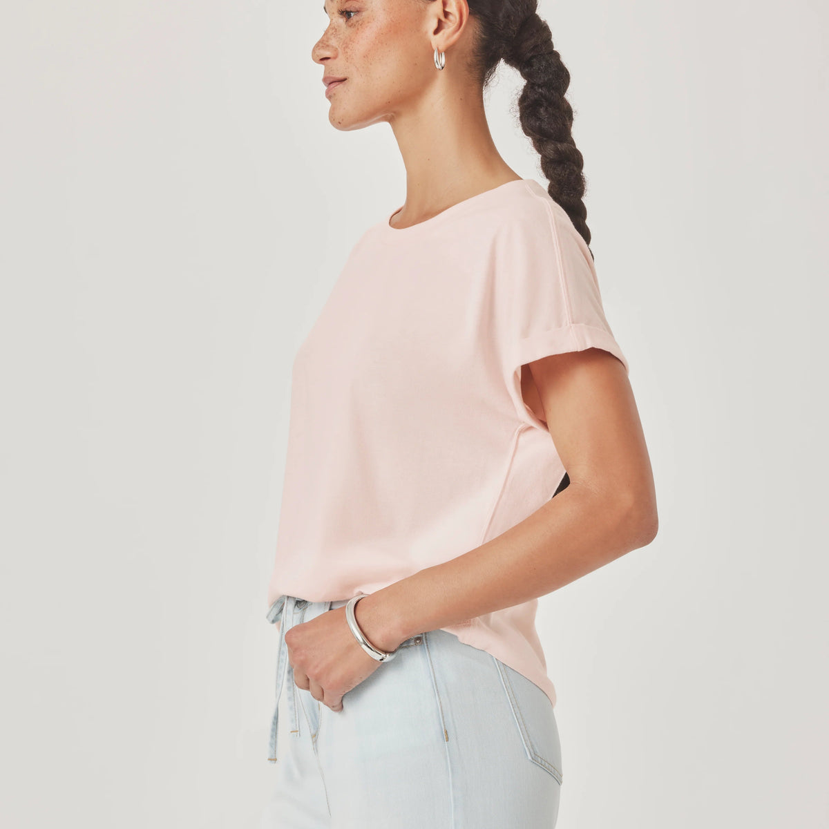 Woman wearing a light pink top and light blue pants against a white background