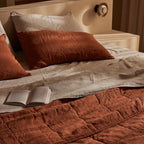 Bed with brown quilt, pillows, and an open book in a warm-toned room.