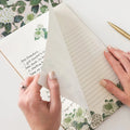 Person holding a letter with floral stationery and a pen on a white surface