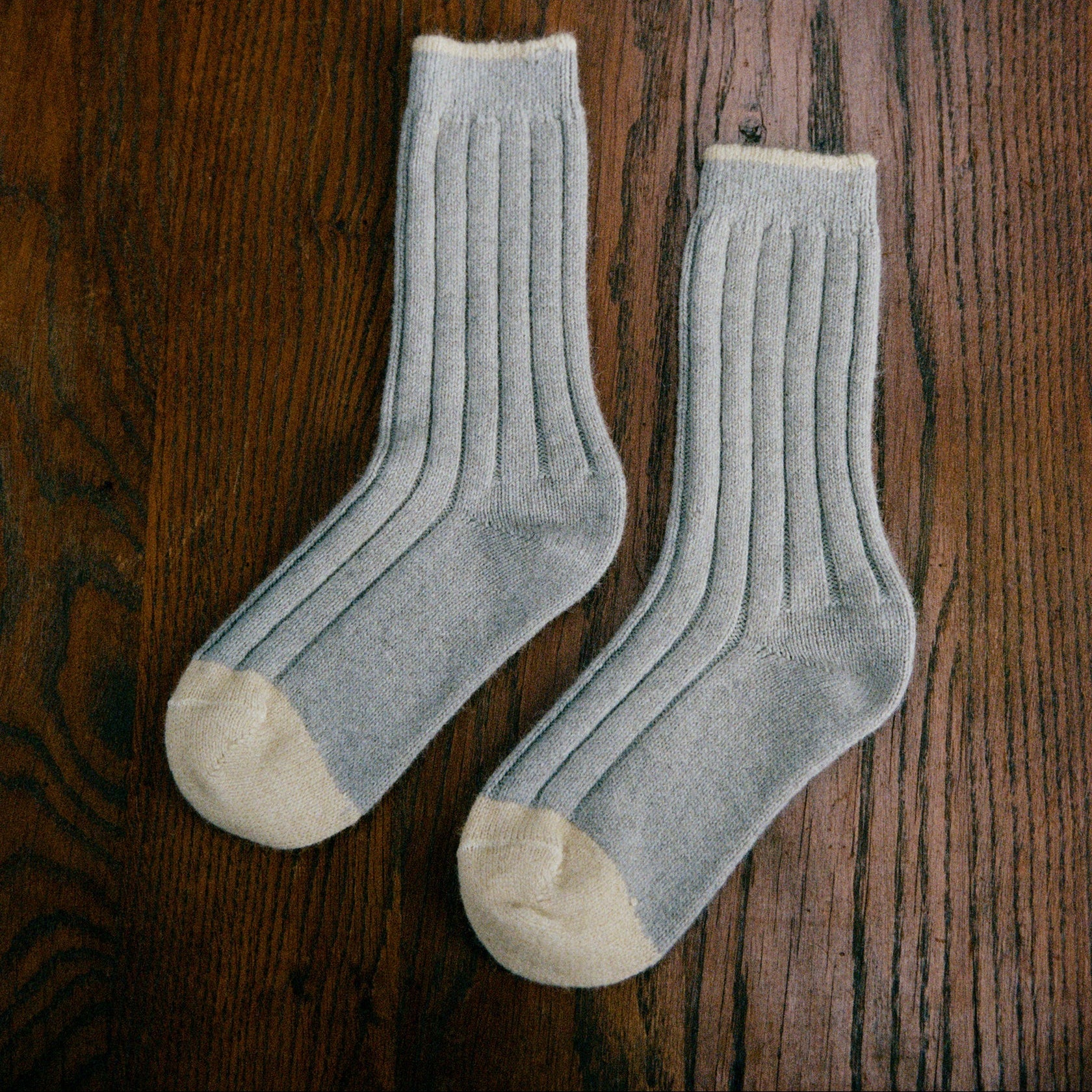 Pair of light gray socks with beige toes and heels on a wooden surface