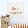 Decorative sign with 'little brother' text, woven basket, and plush caterpillar toy on a wooden surface.