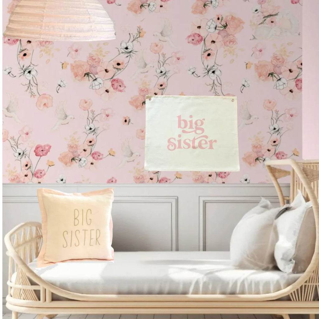 Children's room with floral wallpaper, 'big sister' pillows, and a crib.