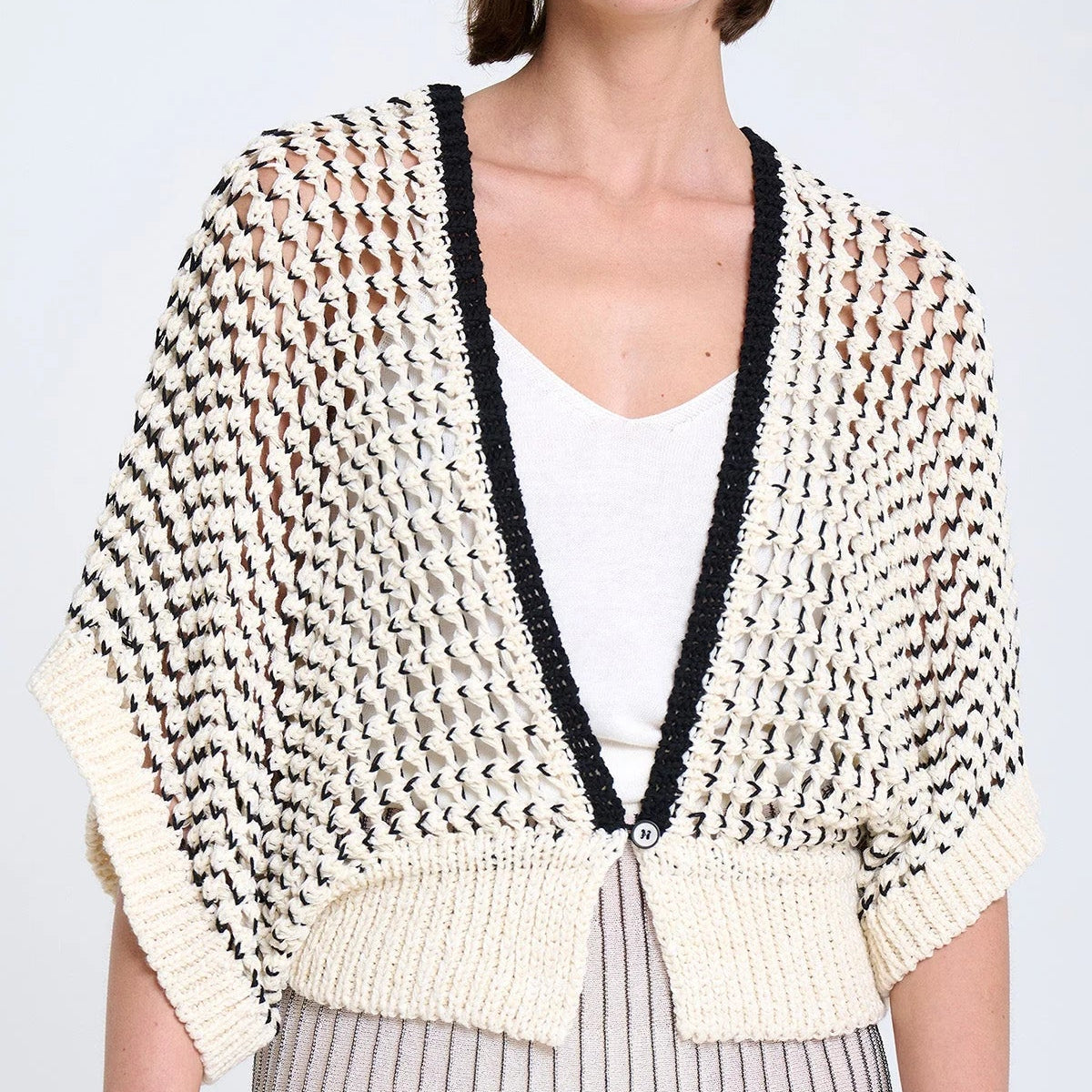 Woman wearing a patterned cardigan over a white top and striped skirt on a light background